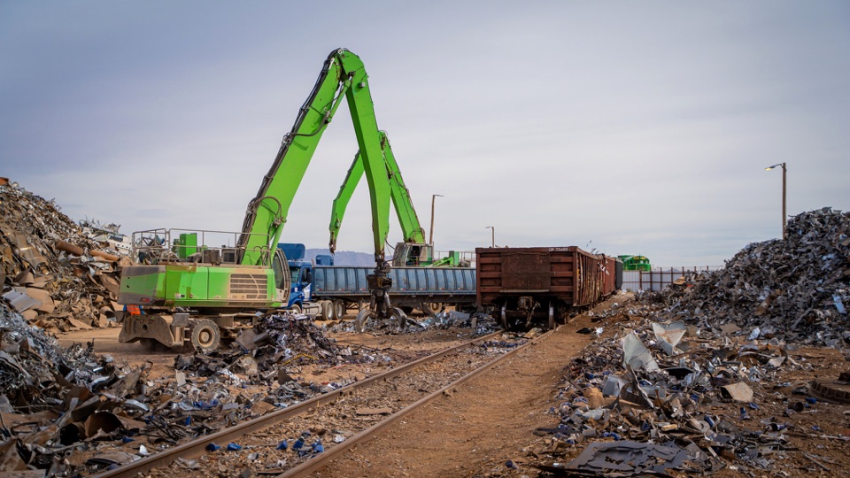 Material handlers beside a railcar in a scrap-metal yard