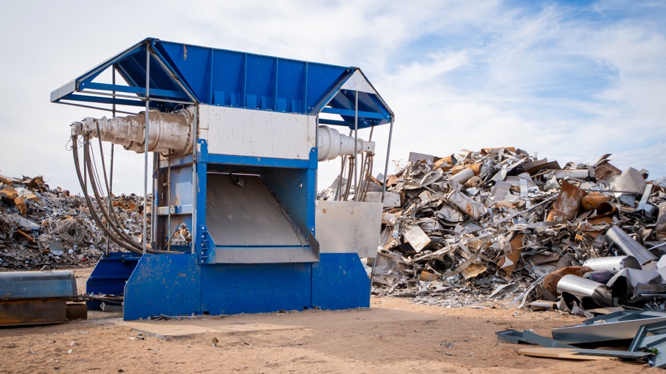 Blue processing equipment beside piles of scrap metal