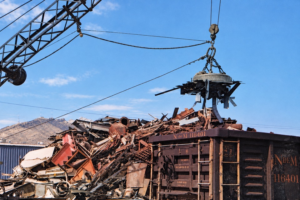 Crane magnet lifting scrap beside a railcar — AI-restored archival image
